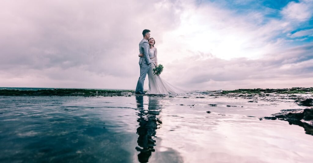 A joyful couple embracing on the beach in wedding attire under a dramatic sky.